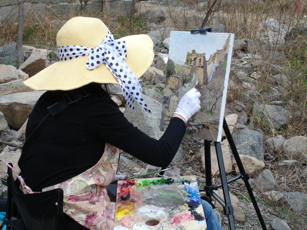 Femme avec un chapeau peignant sur une toile posée surson chevalet